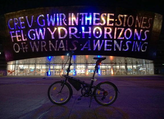 Ein Faltrad steht bei Dunkelheit vor dem Wales Millennium Centre und ist von der linken Seite zu sehen. 