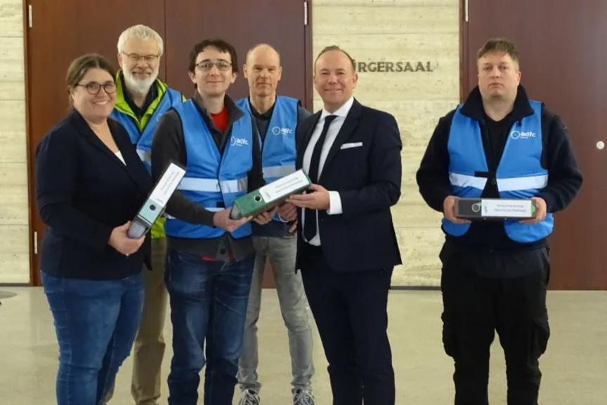Übergabe der Unterschriften an Bürgermeister Daniel Fluhrer Das Foto zeigt mehrere Personen, die Herrn Bürgermeister Daniel Fluhrer drei Aktenordner übergeben und dabei in die Kamera schauen.